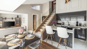A modern kitchen with a central island, a dining area with a table set for four, and a staircase leading to an upper level. - Nardi Nişantaşı (Istanbul)