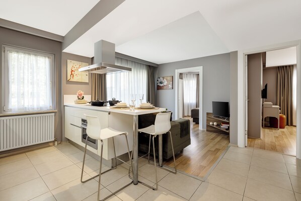 A modern kitchen with white bar stools, a dining table, and a built-in oven. There is a TV and a bookshelf in the adjacent living area. - Nardi Nişantaşı (Istanbul)