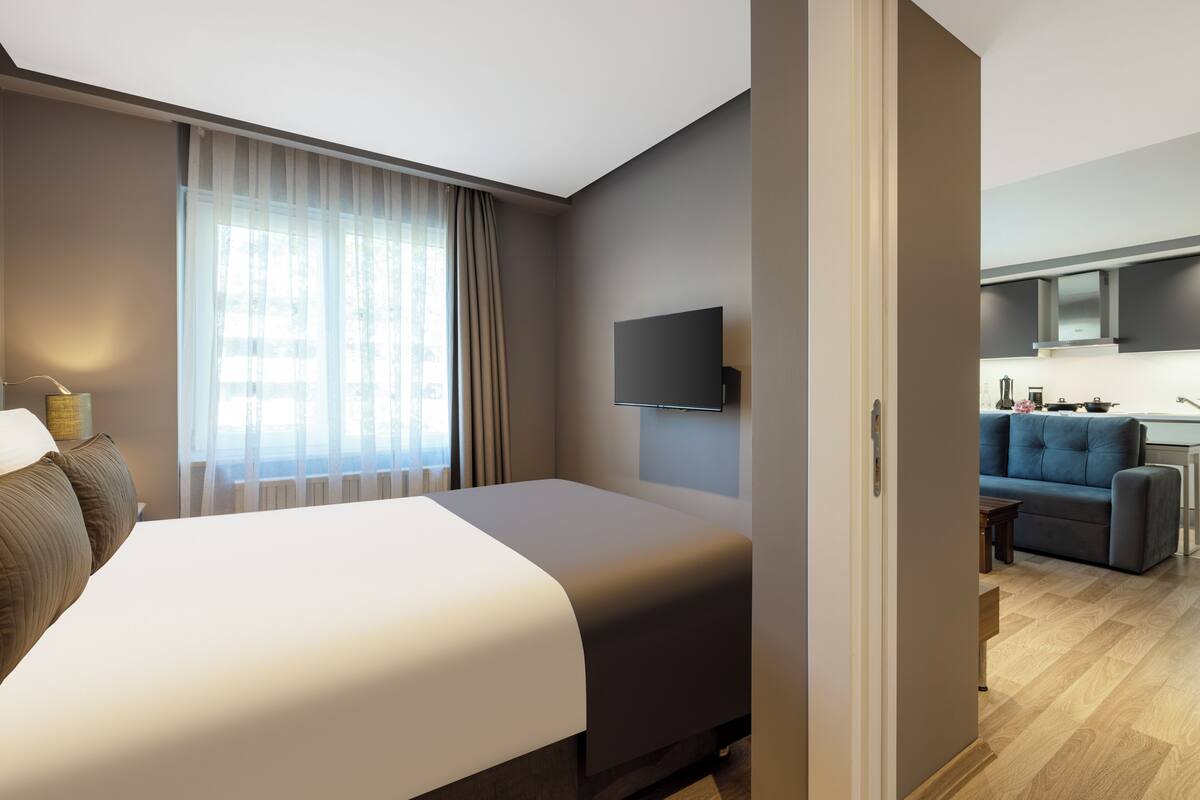 Quarto de hotel moderno com uma cama grande, uma televisão de tela plana na parede e vista para a área da cozinha.