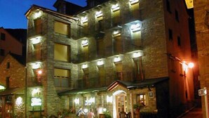 A multi-story stone building with illuminated windows and a ground-floor entrance. - Hotel Gabarre (Broto)