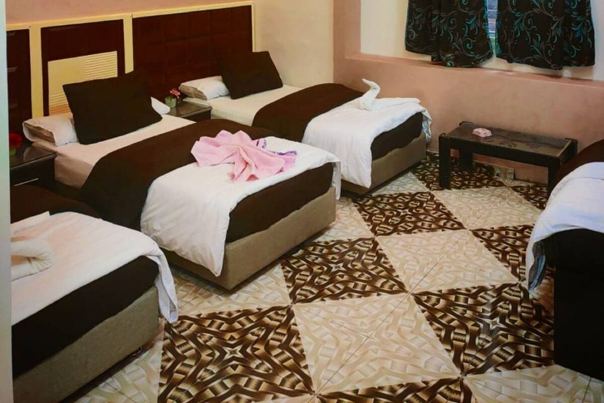 A hotel room with two beds, a patterned floor, an air conditioning unit, and a window with curtains.