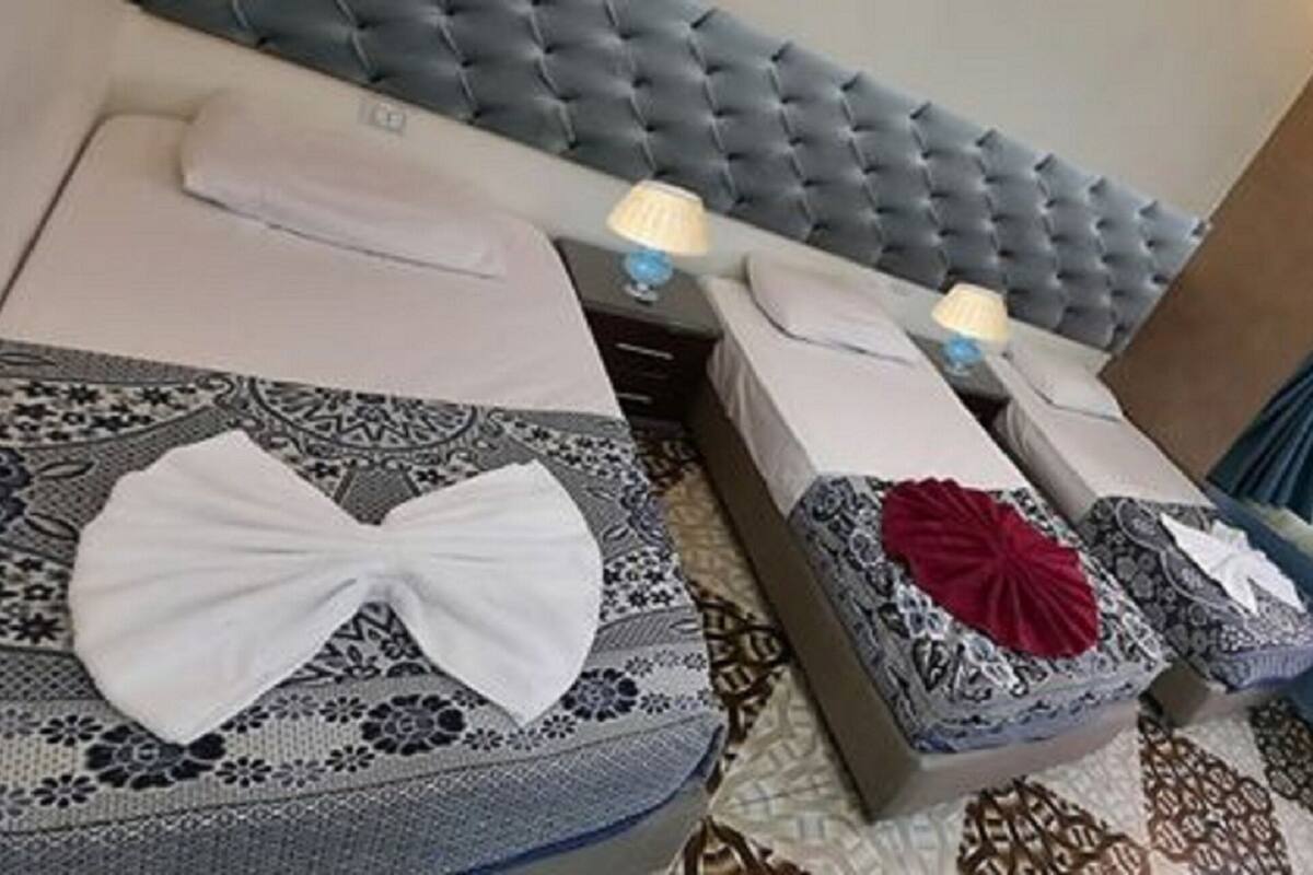 A hotel room with two beds, each with a decorative bow on the pillows, a tufted headboard, and a window with curtains.