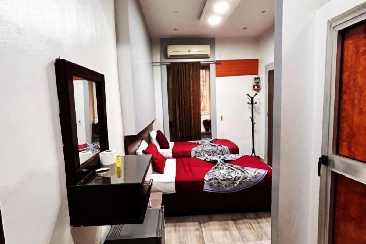 A narrow hotel room with a bed, a desk, a mirror, and an air conditioning unit.