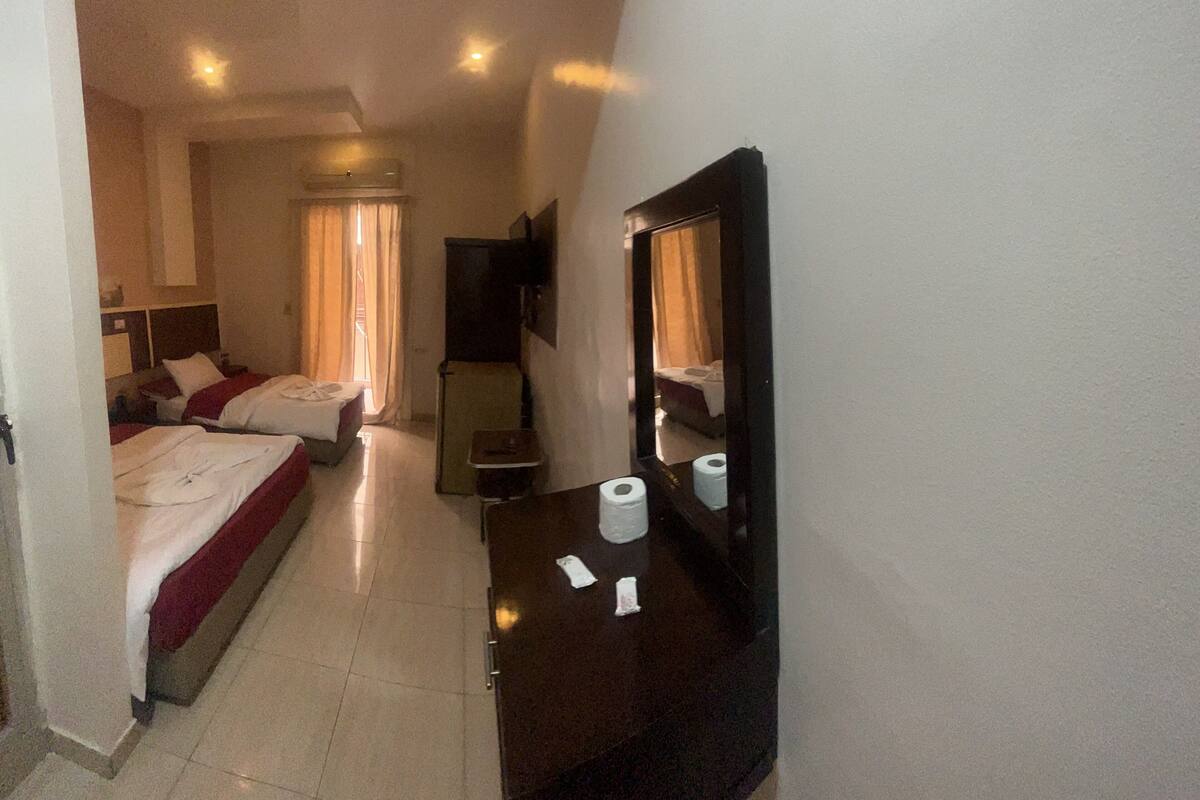 A hotel room with two beds, a desk, a mirror, a TV, and a bathroom visible through an open door.