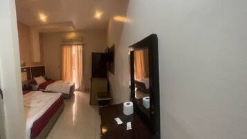 Habitación de hotel con dos camas, un escritorio, un espejo, un televisor y un baño visible a través de una puerta abierta.