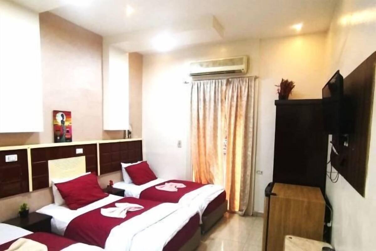 A hotel room with two beds, an air conditioning unit, a television, and a small table.