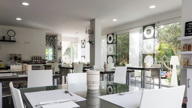 A modern kitchen with white chairs, a glass table, and a view of greenery outside. - Villa Liliana (Cervia)