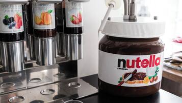 Un distributeur de Nutella avec plusieurs pots de différentes saveurs, une cuillère et de petits gobelets, le tout posé sur un comptoir noir.