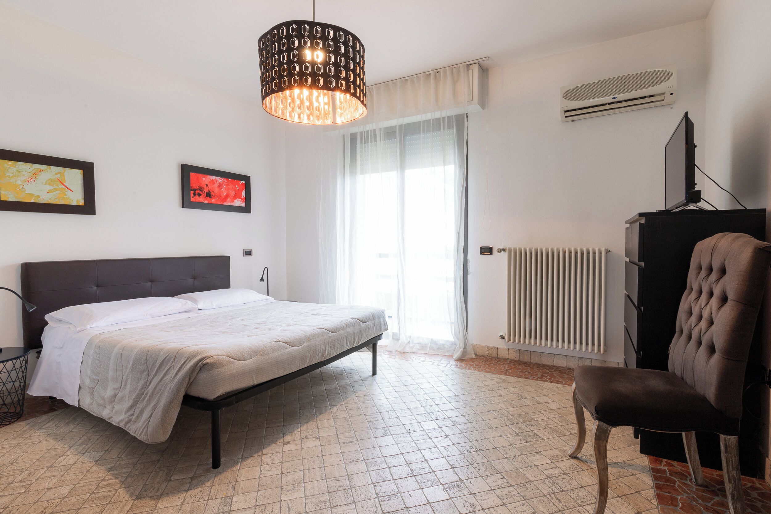 Ein Schlafzimmer mit Bett, Sessel, Heizkörper und Fernseher.