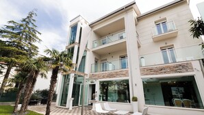 A modern multi-story building with balconies, a glass entrance, and outdoor seating. - Villa Liliana (Cervia)