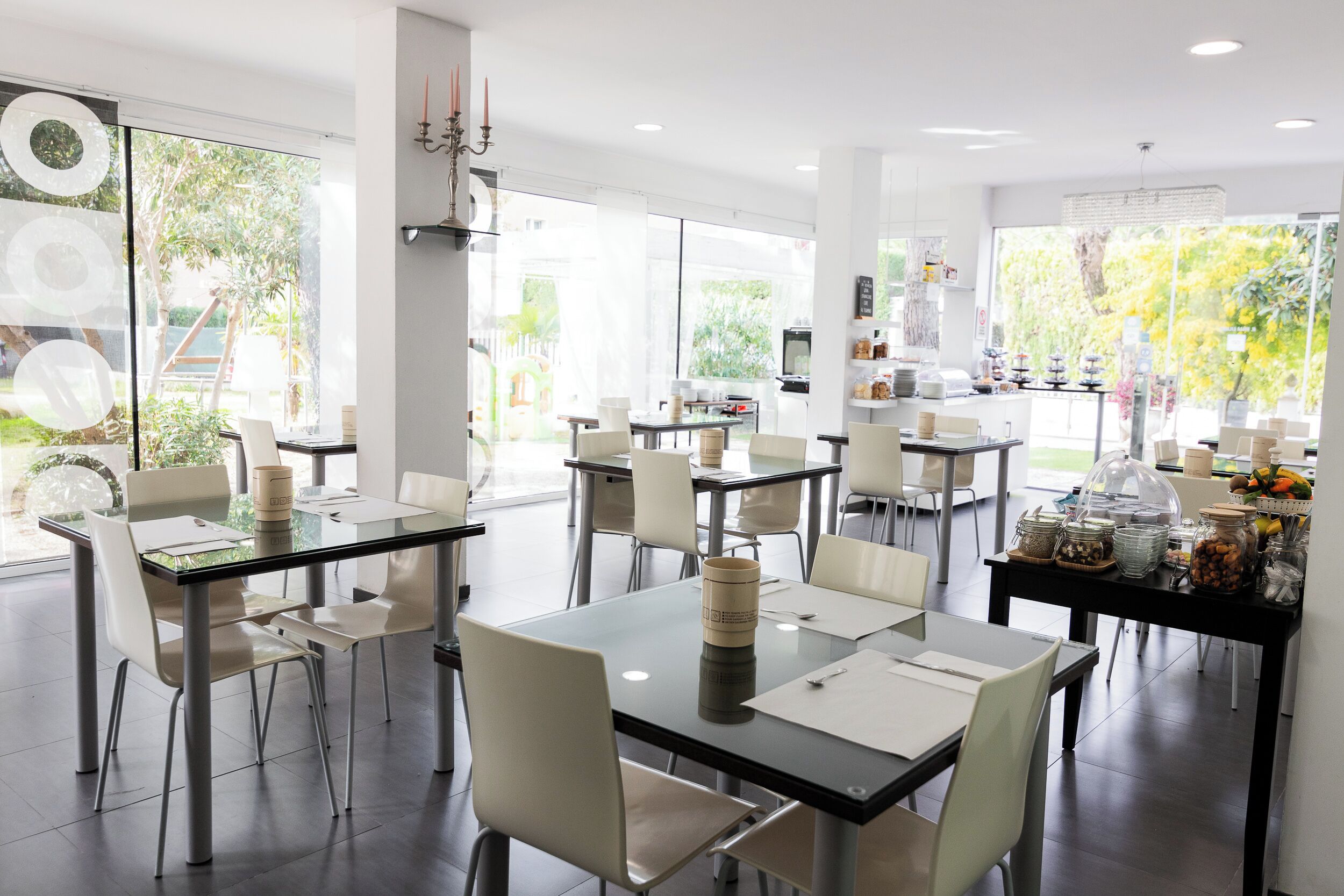 Un comedor moderno con mesas de vidrio, sillas blancas y un bufé con diversas opciones de comida.