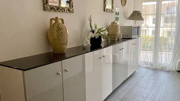 Una cocina moderna con encimera negra, armarios blancos y jarrones decorativos. Hay dos espejos en la pared y una ventana con cortinas de gasa.