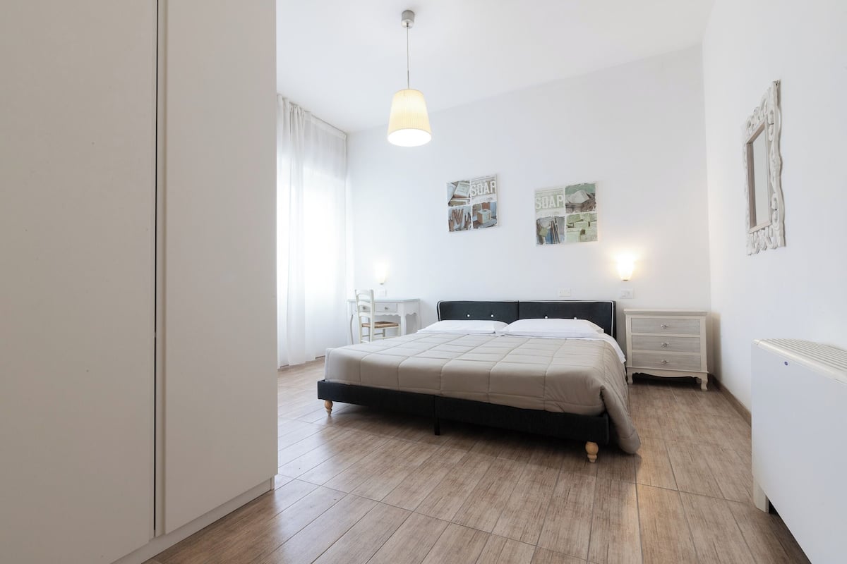 A bedroom with a bed, bedside tables, a wall-mounted light fixture, and a radiator.