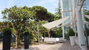 An outdoor patio area with a tiled floor, a white umbrella, and a seating arrangement. - Villa Liliana (Cervia)