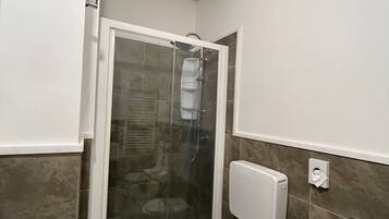 A bathroom with a shower enclosure, toilet, and towel rack.