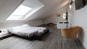 A modern bedroom with a skylight, a bed, a bench, a chair, and a TV. - Villa Liliana (Cervia)