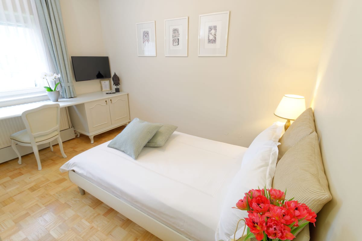 A bedroom with a bed, a desk, a chair, a TV, and framed pictures on the wall.