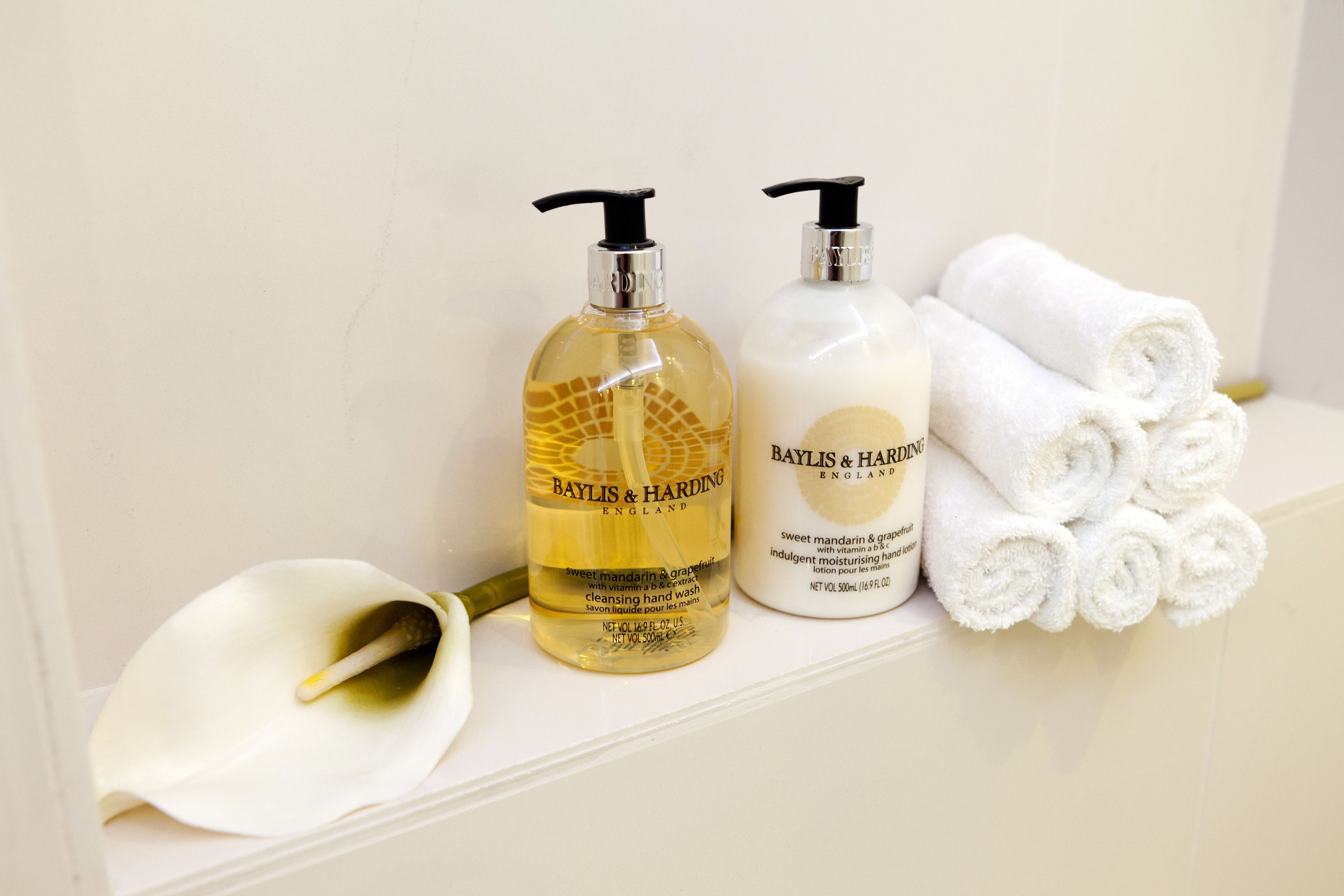 Zwei Flaschen Baylis & Harding Handseife und ein Stapel weiße Handtücher auf einem Regal.