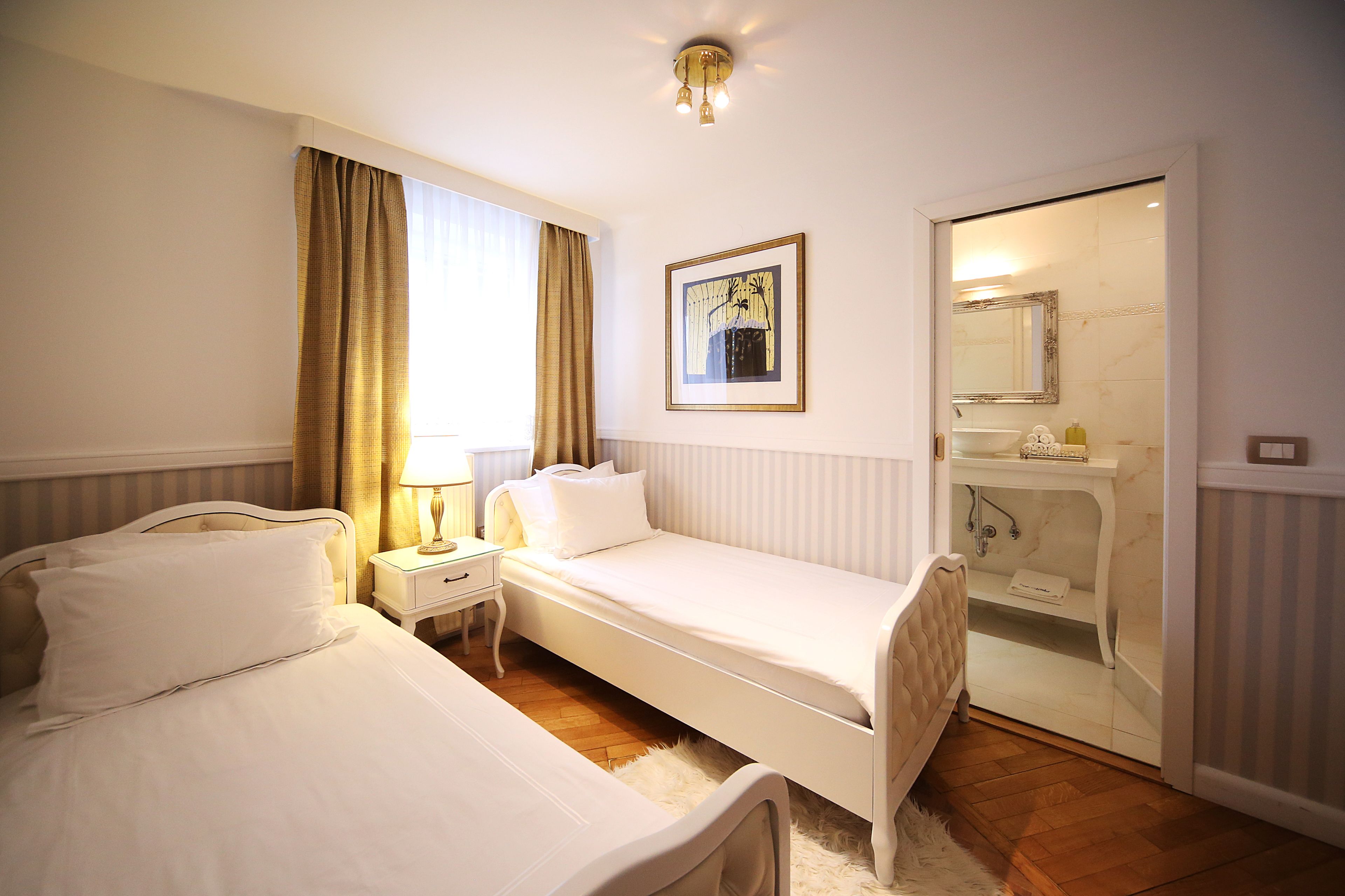 A hotel room with two beds, a bedside table with a lamp, a framed picture on the wall, and a bathroom visible through an open door.