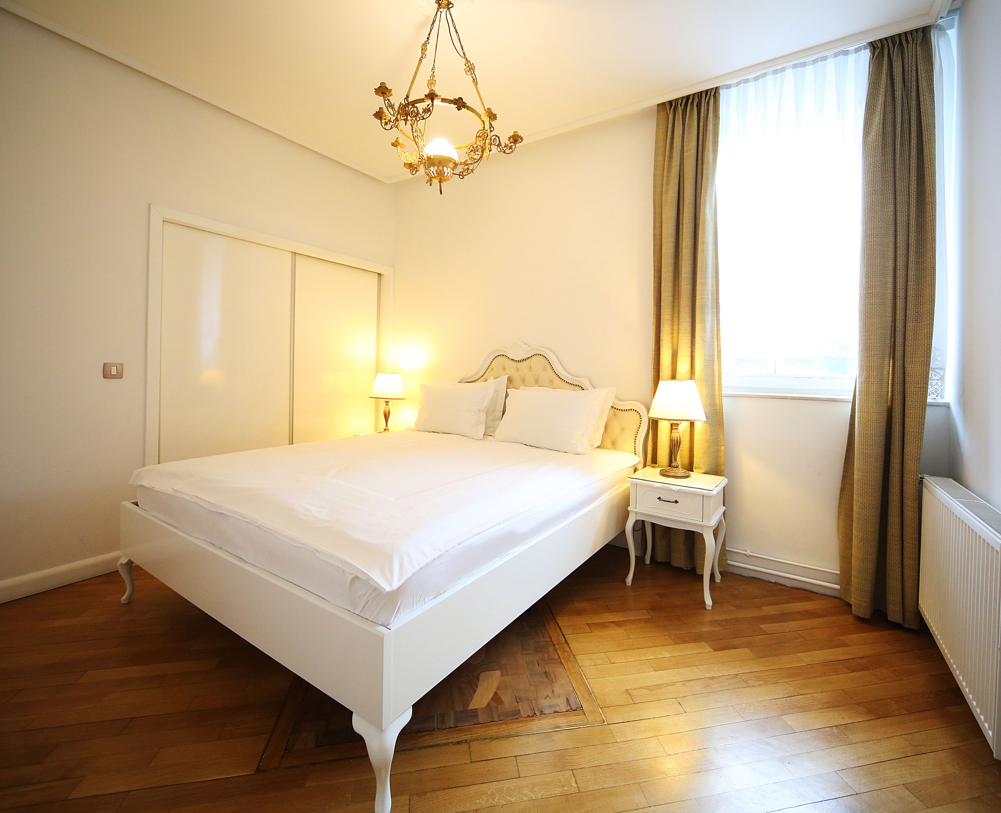 A neatly arranged bedroom with a large bed, bedside lamps, and a chandelier.