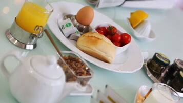 A breakfast setting with a teapot, a glass of orange juice, a plate with eggs, tomatoes, and bread, and condiments on a table.