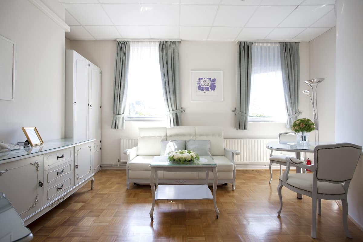 A well-lit living room with a white sofa, a glass coffee table, and a white cabinet with drawers.