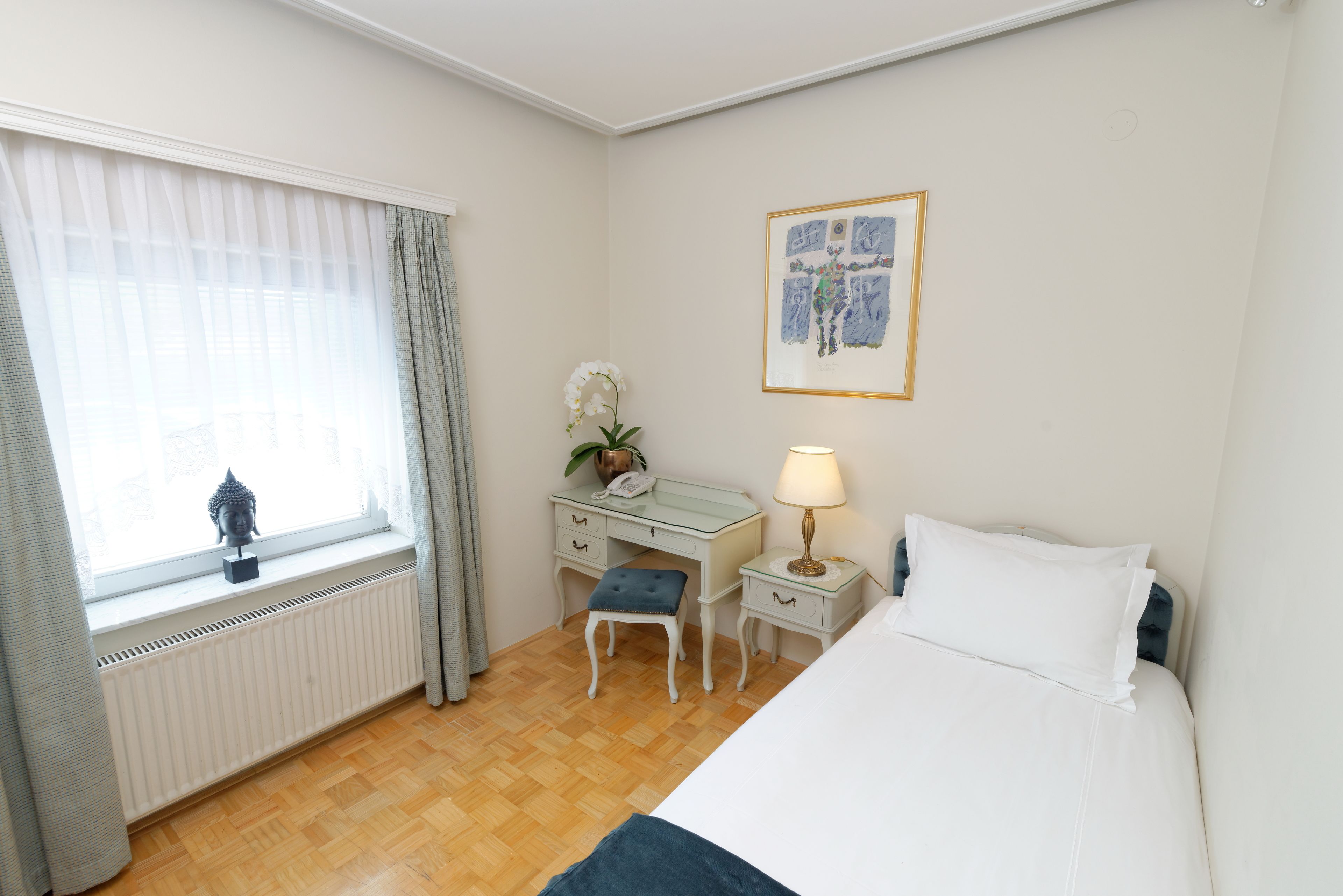 Hotellihuone, jossa on sänky, työpöytä, tuoli, patteri, ikkuna verhoilla ja seinälle ripustettu taulu.