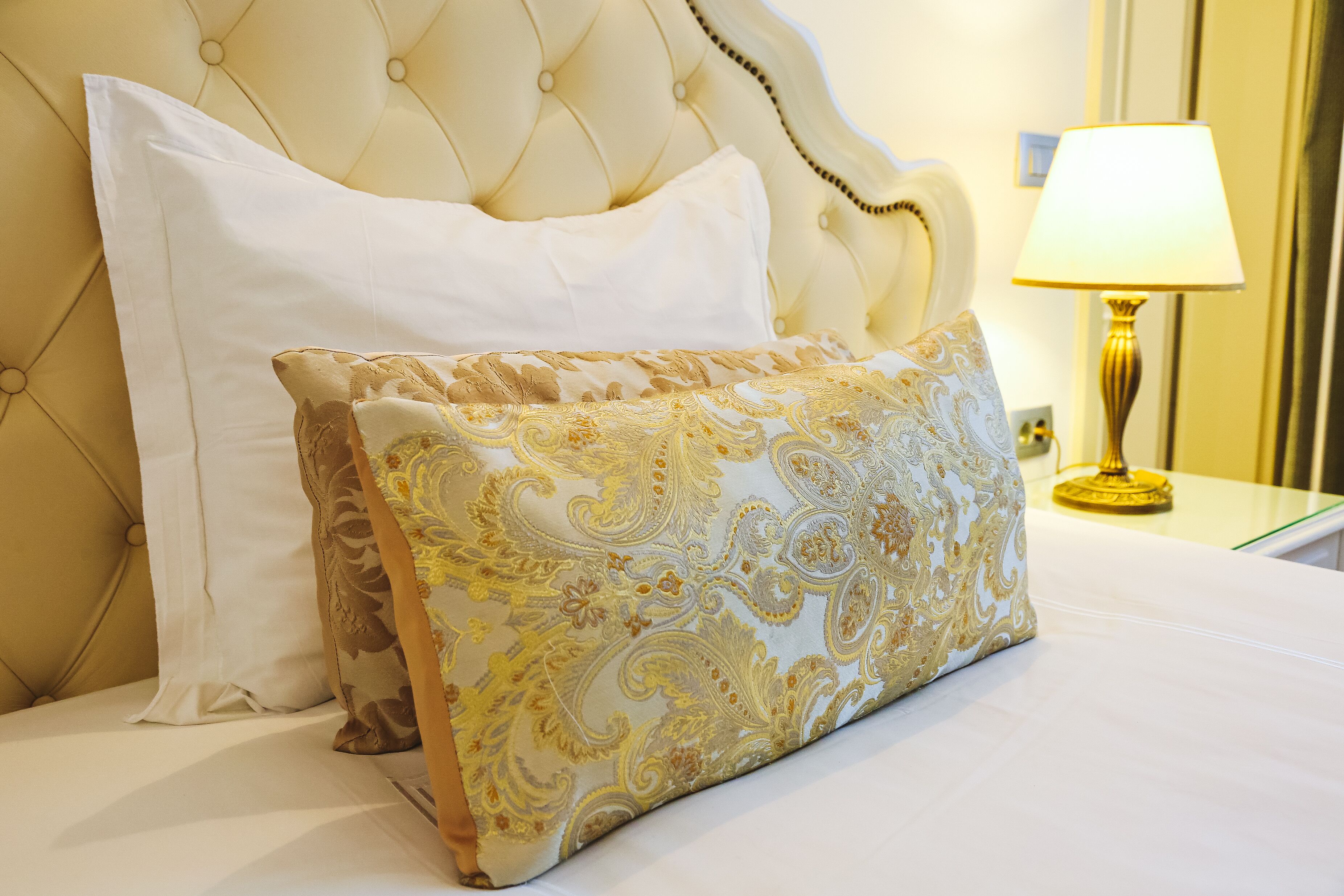 A bed with a tufted headboard, two pillows, and a bedside table with a lamp.