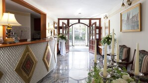 A hotel lobby with a reception desk, a chandelier, a large mirror, and a view through a glass door. - Aparthotel Vila Minka (Ljubljana)