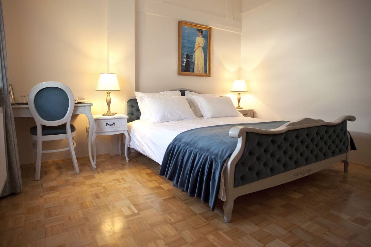 A bedroom with a bed, two bedside tables with lamps, a chair, and a painting on the wall.