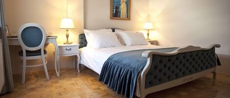 A bedroom with a bed, two bedside tables with lamps, a chair, and a painting on the wall.