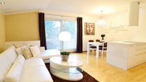 A modern living room with a white sofa, a glass coffee table, and a dining area with a white table and chairs. - Aparthotel Vila Minka (Ljubljana)