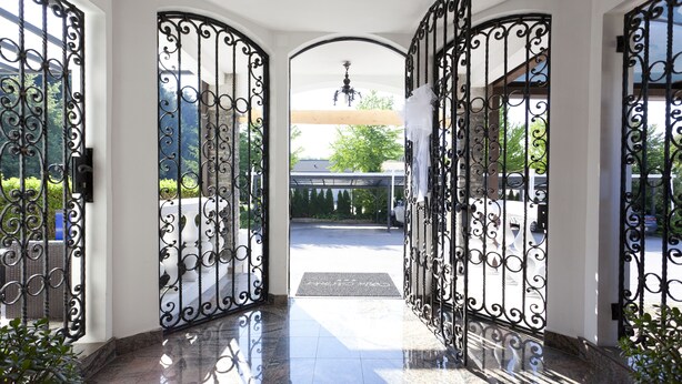 A grand entrance with ornate black metal gates leading to a covered area with a bench and a chandelier. - Aparthotel Vila Minka (Ljubljana)
