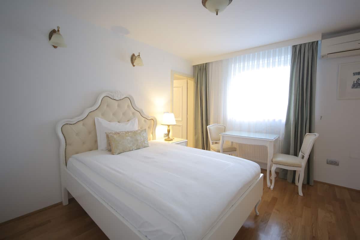 A hotel room with a large bed, a desk, a chair, and a window with curtains.