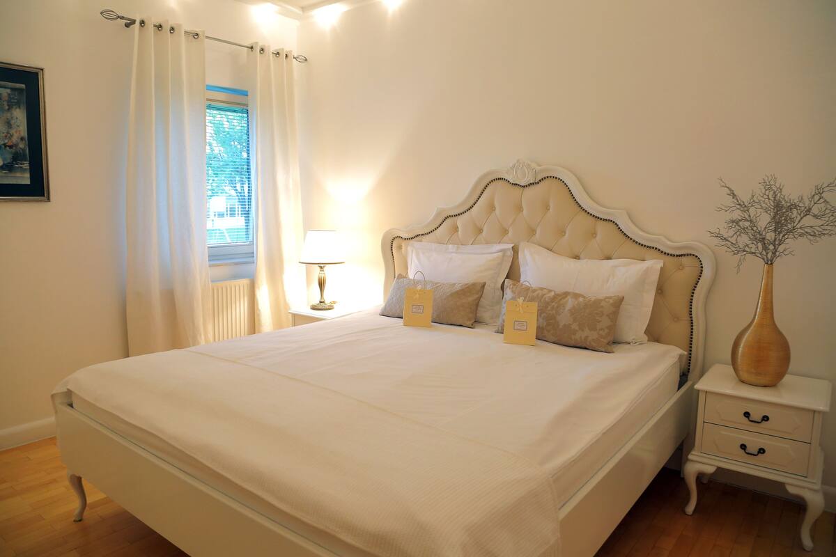 A neatly made bed with a headboard, a bedside table with a lamp, and a vase on a nightstand.