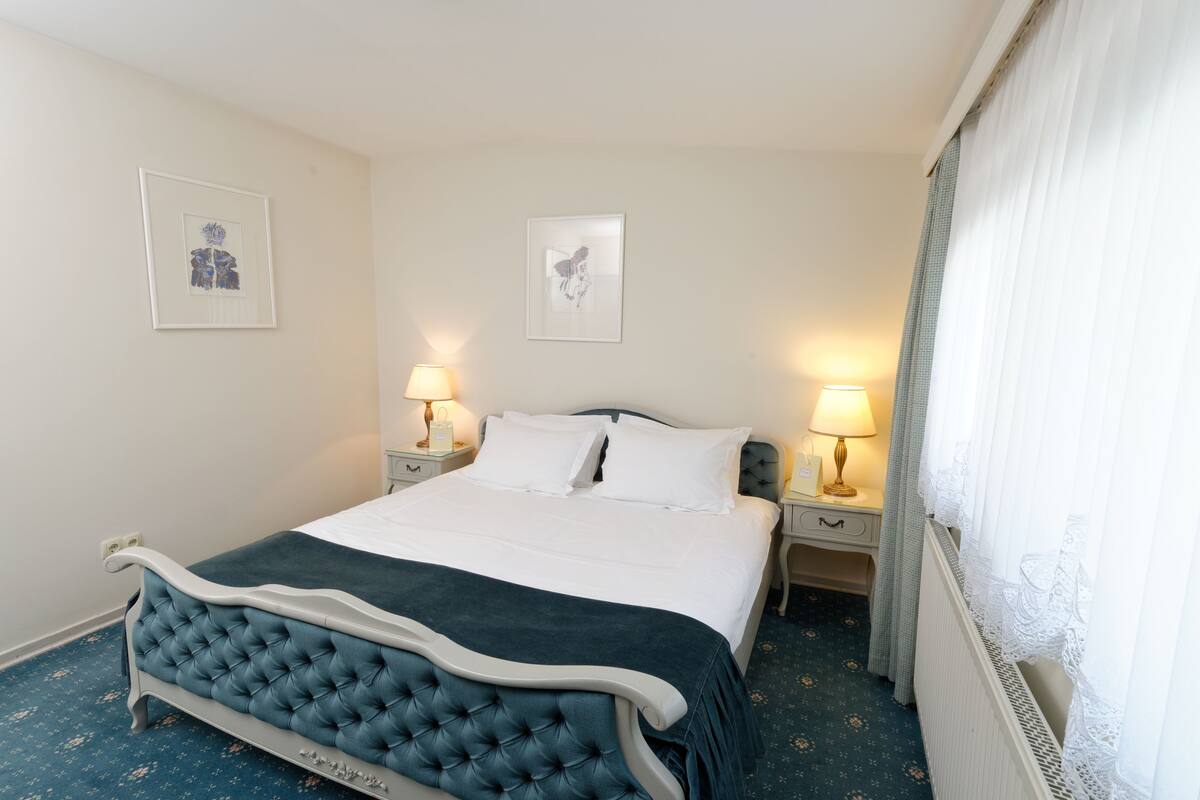 A neatly made bed with a tufted headboard, two bedside tables with lamps, and framed artwork on the walls.