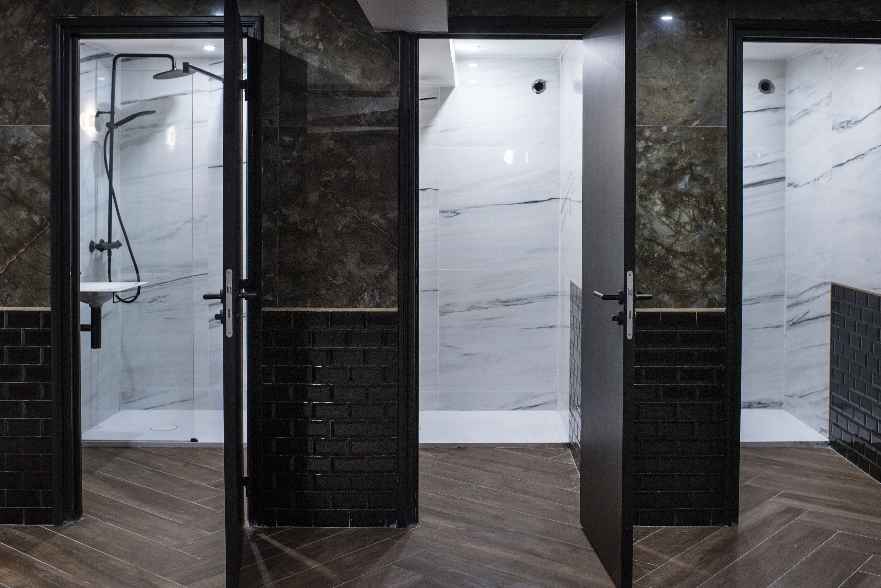 A modern bathroom with a glass-enclosed shower, marble walls, and a wooden floor.