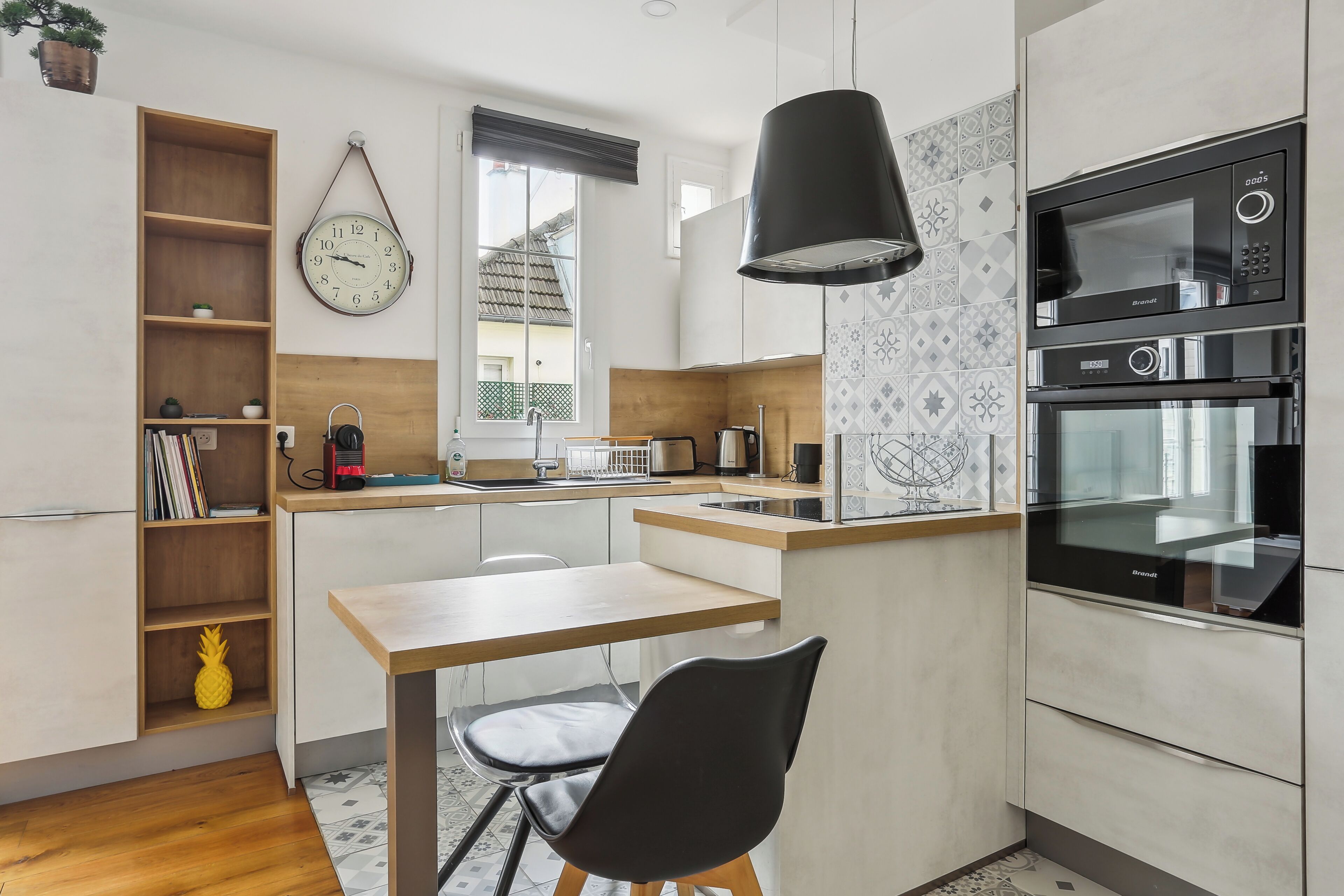 A modern kitchen with a wooden table, black chair, and built-in appliances.