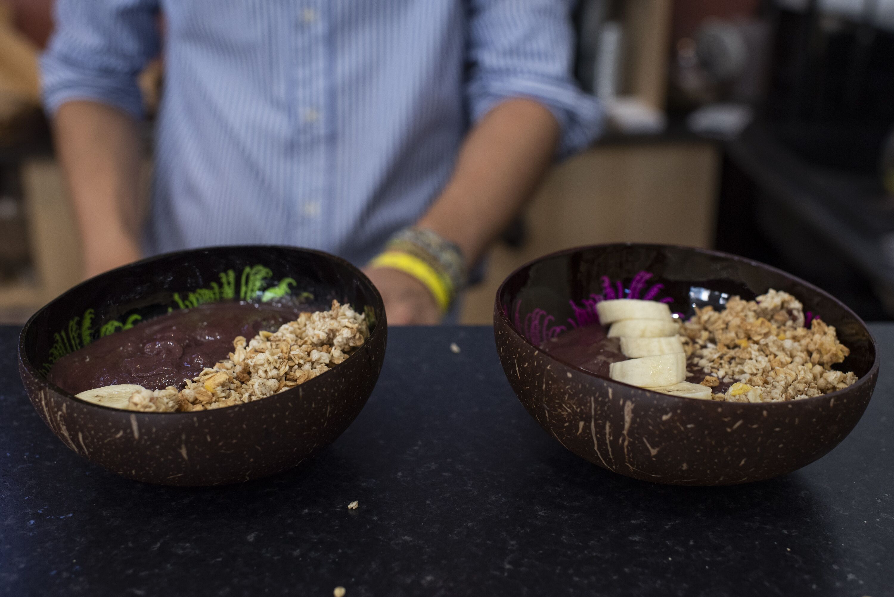 Two bowls of cereal with bananas on a dark countertop.