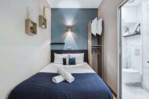 A modern hotel room with a neatly made bed, a wall-mounted light fixture, and a bathroom with a marble sink and shower. - Résidence Aurmat Appart Hôtel Paris Boulogne (Boulogne-Billancourt)