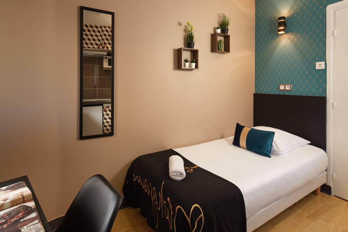 A neatly arranged hotel room with a bed, a chair, a desk, and a mirror.