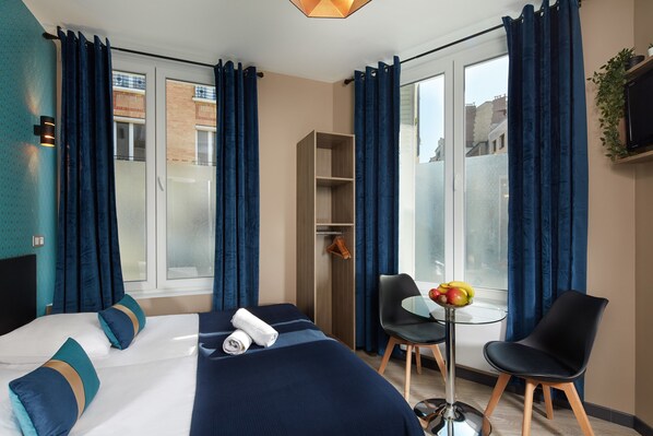 A hotel room with a bed, a desk with a chair, a small table with fruit, and a wardrobe. - Résidence Aurmat Appart Hôtel Paris Boulogne (Boulogne-Billancourt)