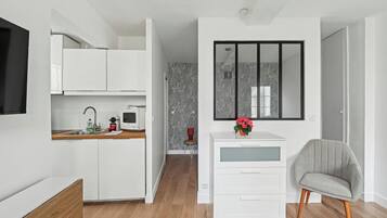 Una cocina moderna con armarios blancos, un microondas y un lavamanos. Hay una pequeña mesa con una silla y un jarrón con flores.