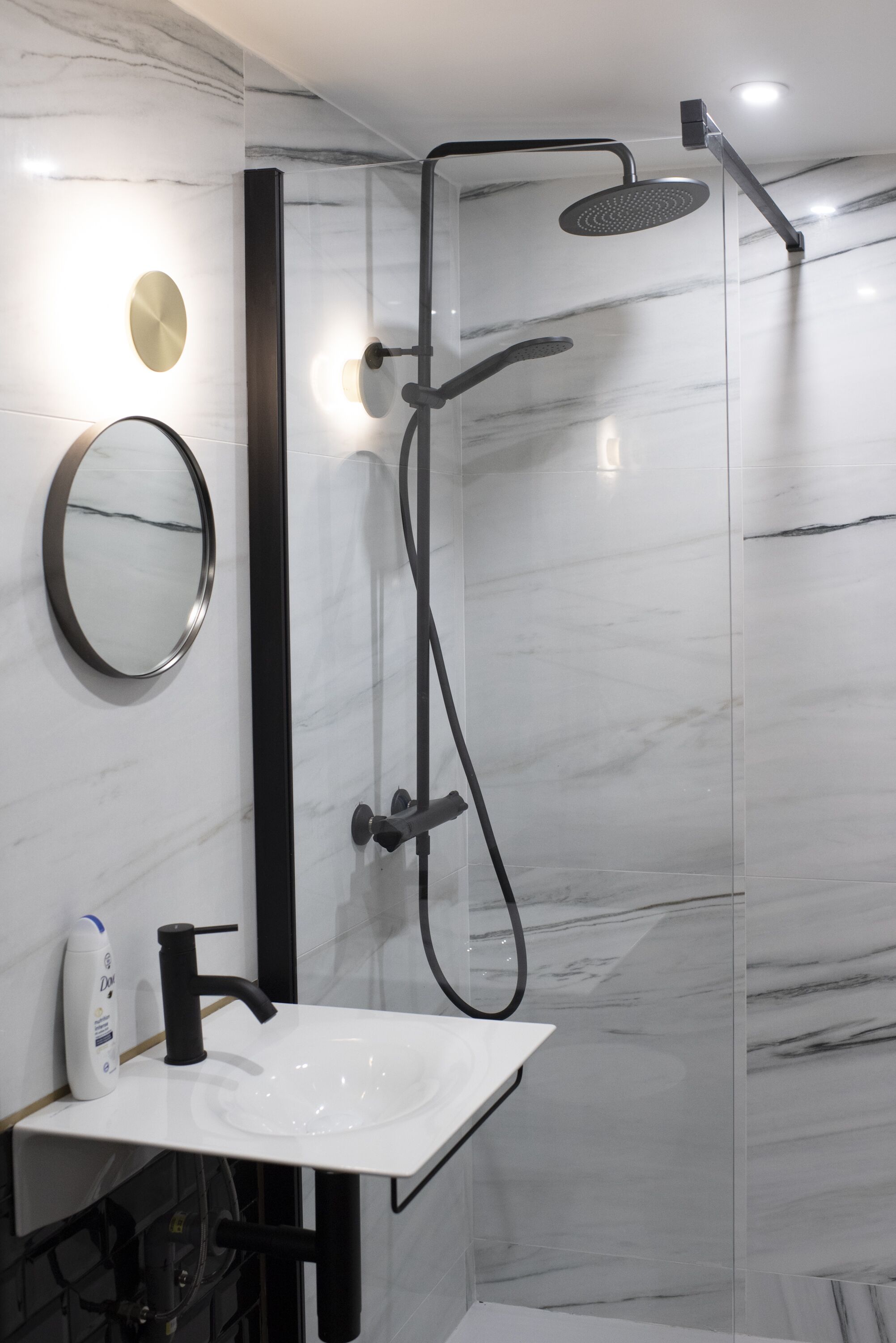 A modern bathroom with a glass-enclosed shower, a white sink with a black faucet, and a round mirror.