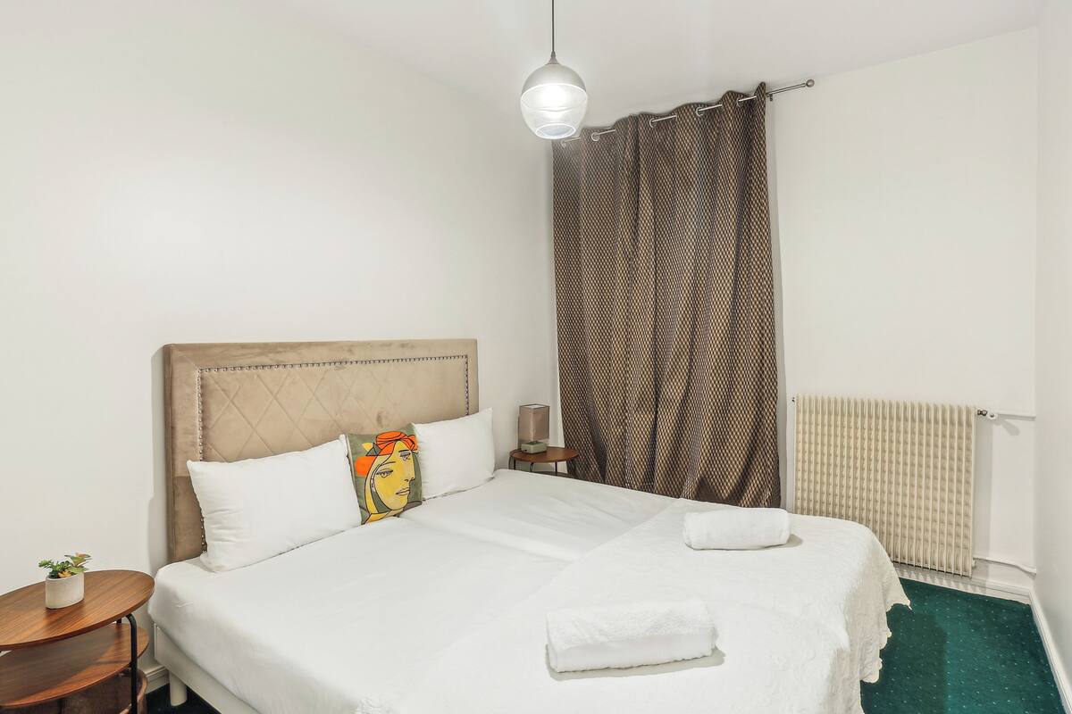 A neatly made bed with white linens, a headboard, and a bedside table with a lamp.