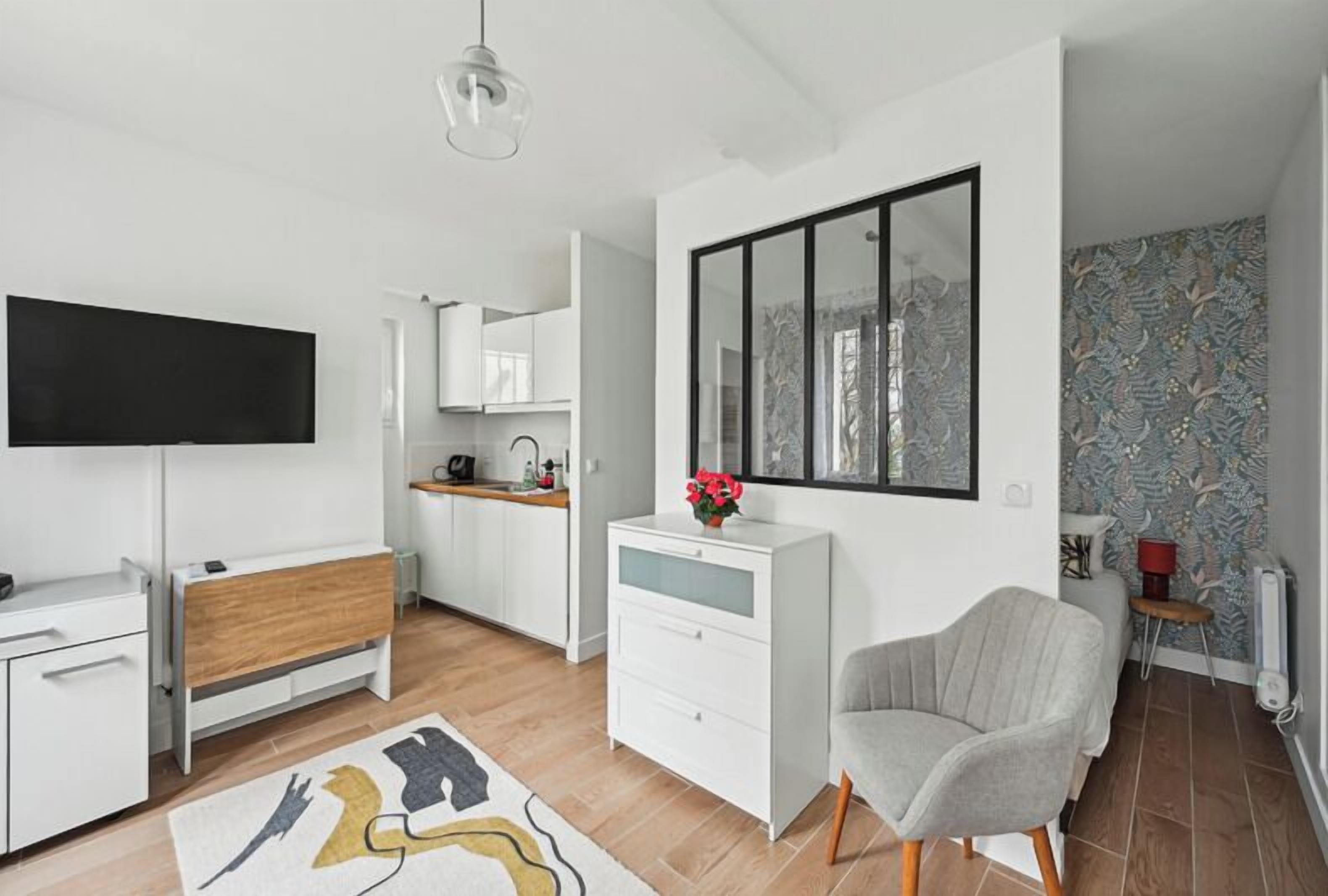 A modern living room with a flat-screen TV, a wooden bench, a white dresser, and a grey armchair.