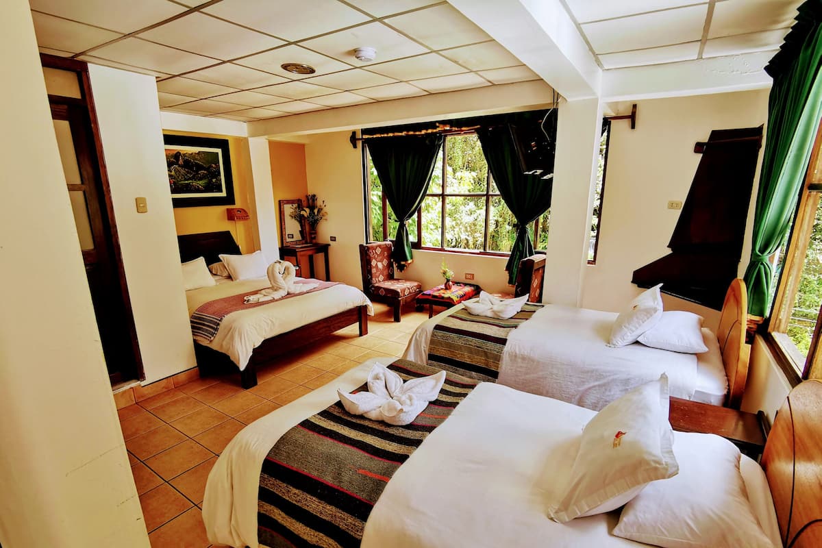 A hotel room with two beds, a small sitting area, and a window with curtains.