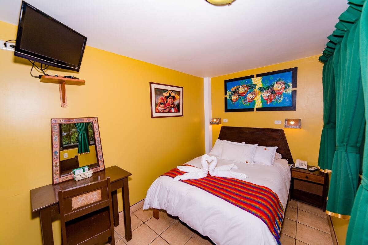 A hotel room with a bed, a desk, a television, and artwork on the walls.