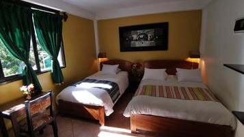 Habitación de hotel con dos camas, una silla, una mesa, un cuadro en la pared y una ventana con cortinas.
