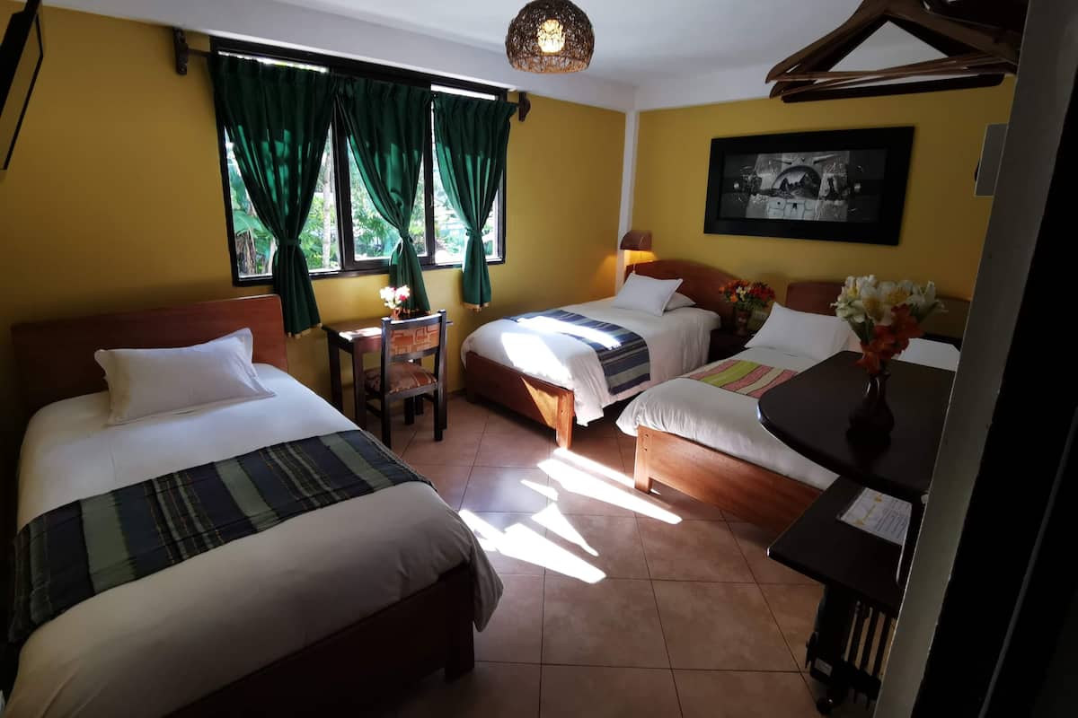 A hotel room with two beds, a small table, a chair, a desk, and a hanging light fixture.